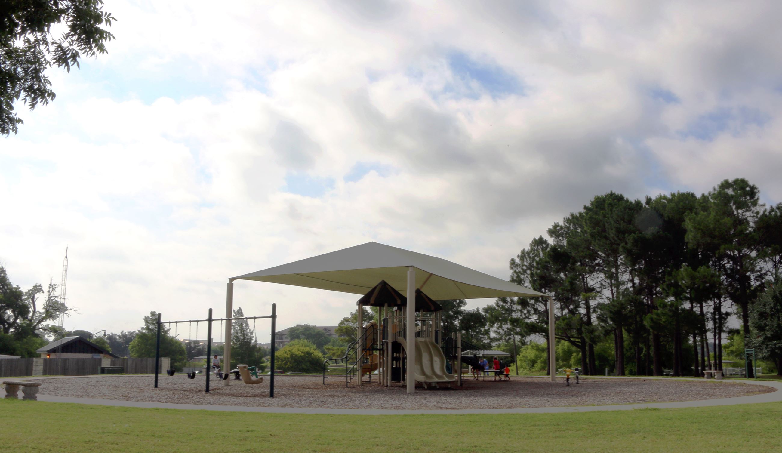 A shaded playground with slides and swings at Granbury's Hewlett Park.